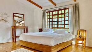 Un dormitorio con una cama de madera, una mesita de noche de madera, un espejo y una ventana con cortinas.