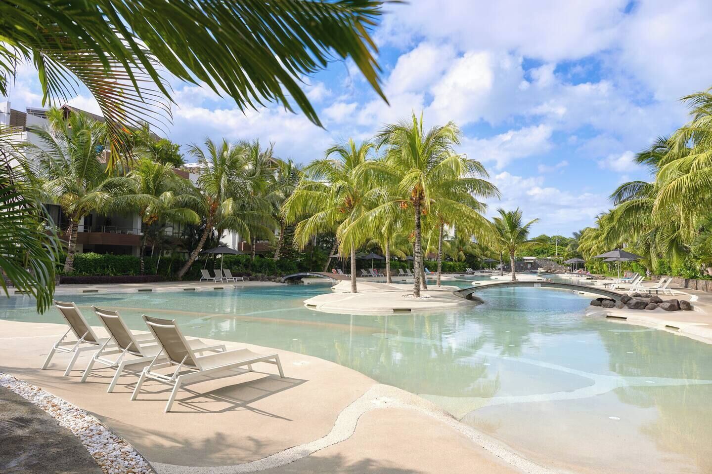 Ein Poolbereich eines Resorts mit Liegestühlen, Palmen und blauem Himmel.