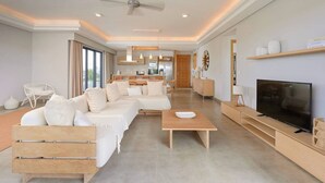 A modern living room with a sofa, coffee table, TV, and kitchen in the background. - Penthouse Blue Horizon, 5 min Mont Choisy beach (Trou-aux-Biches)