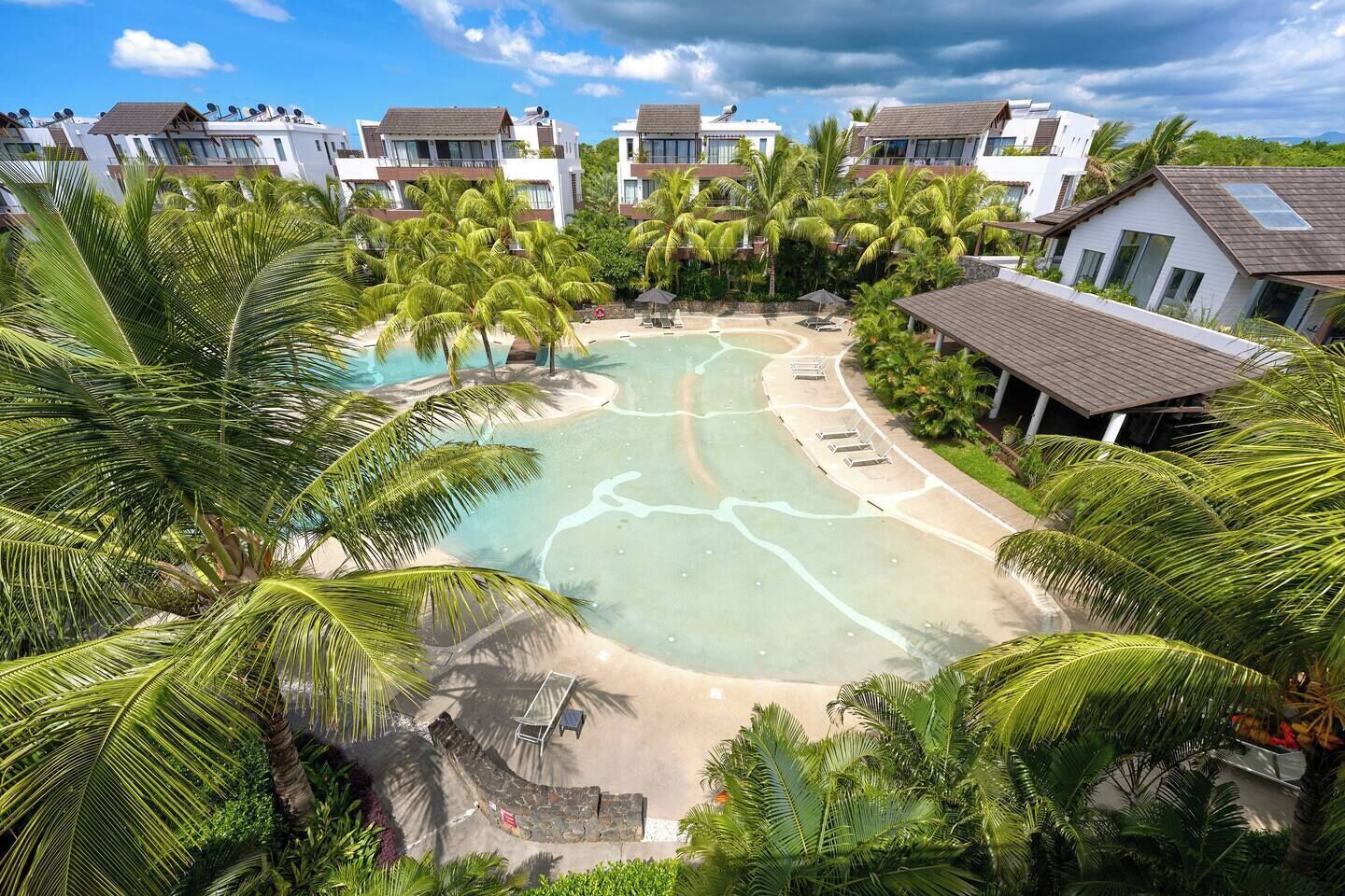 A resort with a central pool, palm trees, and modern buildings.