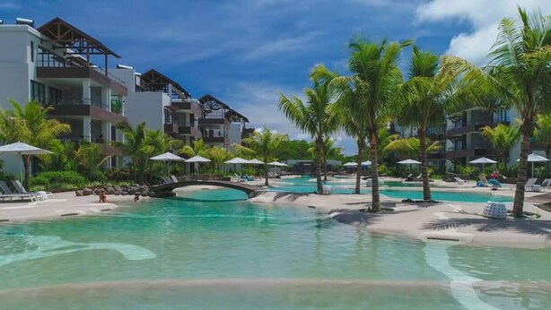 A resort with a central swimming pool, palm trees, and multiple buildings with balconies. - Penthouse Blue Horizon, 5 min Mont Choisy beach (Trou-aux-Biches)