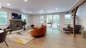 A spacious living room with a stone fireplace, large windows, and a modern sofa. - Relaxing A-Frame with Hot Tub and Lake Access (Denmark)