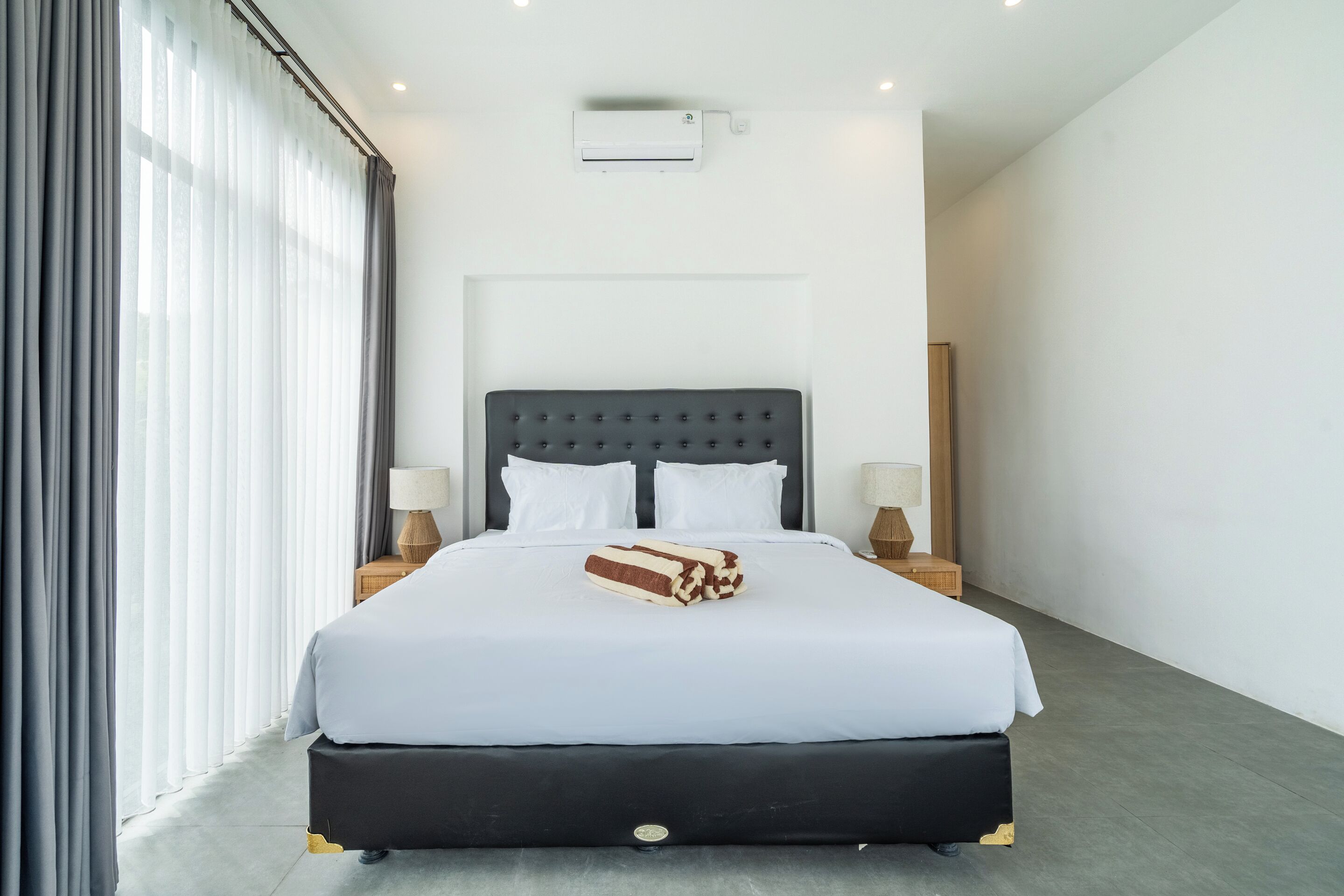 A modern hotel room with a large bed, two bedside lamps, a flat-screen TV, and a window with curtains.