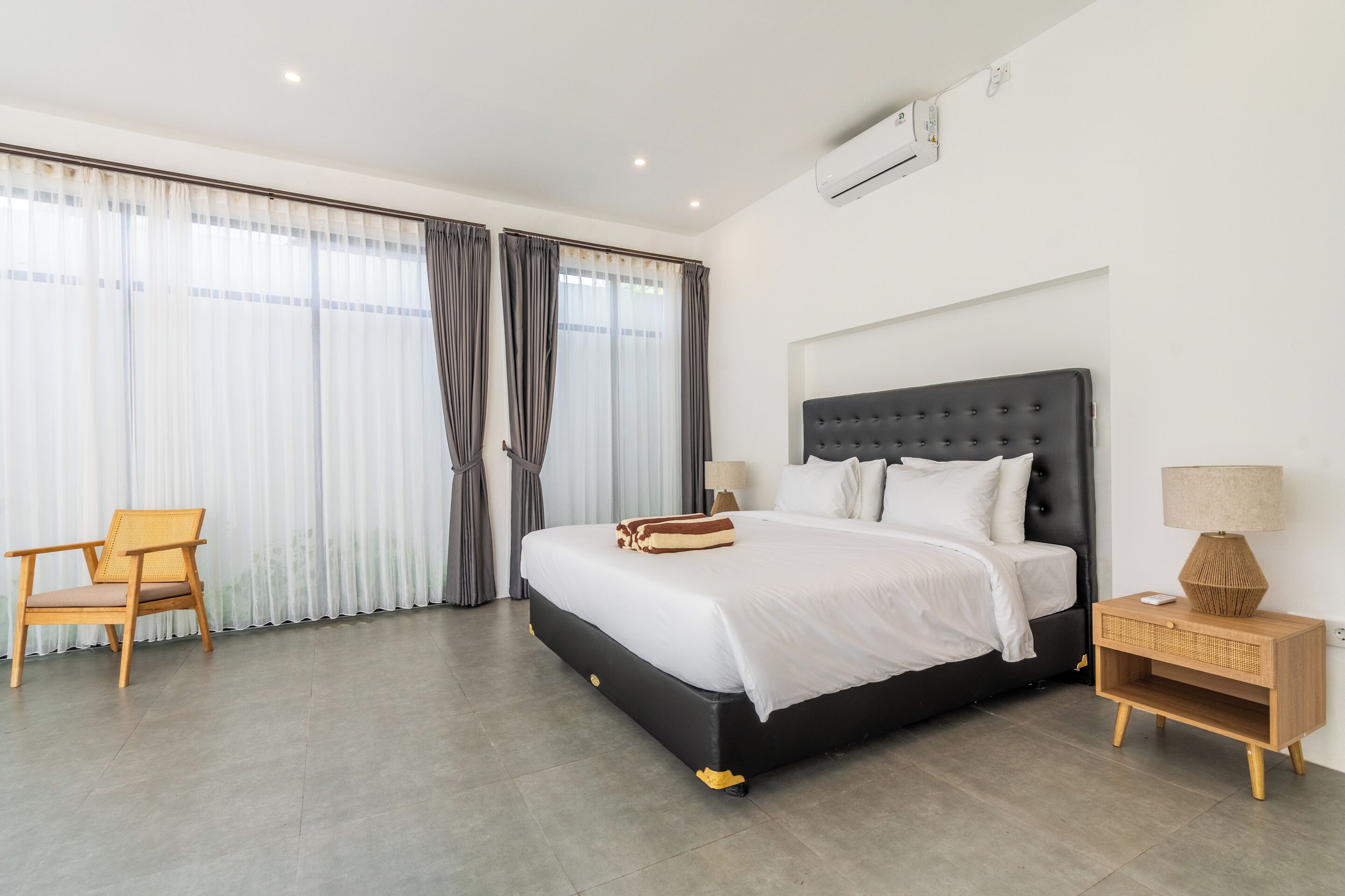 Une chambre d’hôtel moderne avec un grand lit, une chaise en bois et une table de chevet avec une lampe.