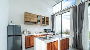 A modern kitchen with a central island, wooden cabinets, a built-in microwave, and a large window with curtains. -  Light Way Villa in Canggu (Canggu)