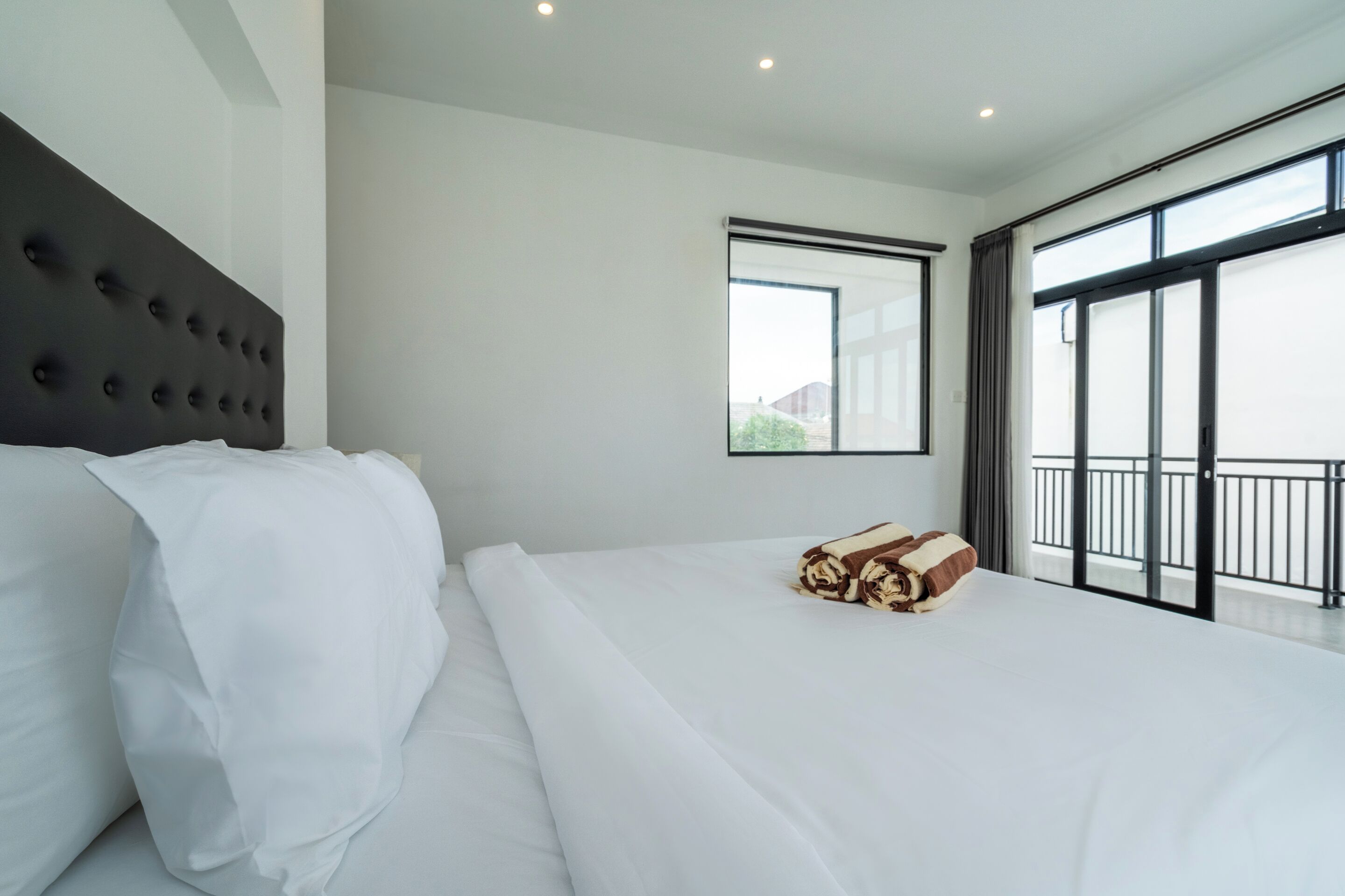 A modern hotel room with a large bed, a headboard, a window with a view, and a balcony.