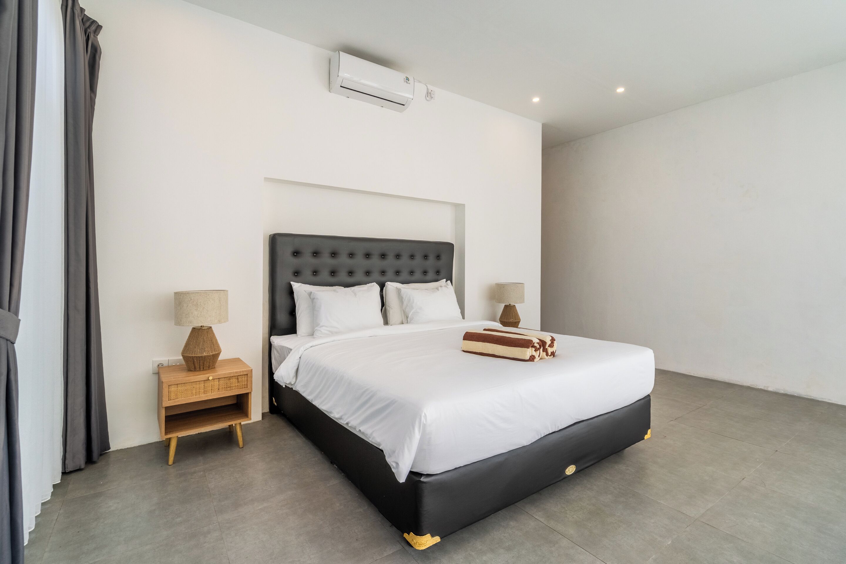 A modern bedroom with a large bed, a bedside table, and a wall-mounted air conditioner.