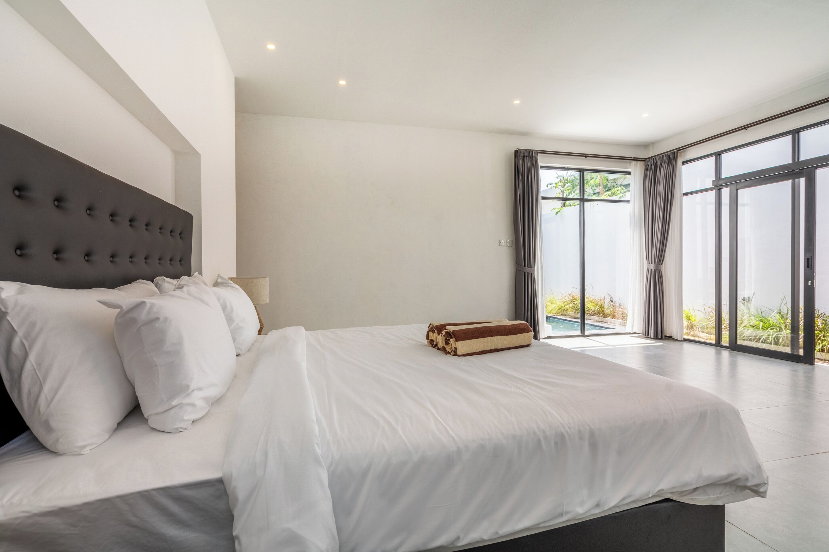 Ein modernes Schlafzimmer mit einem großen Bett, einem Kopfteil und Blick ins Freie durch große Fenster.