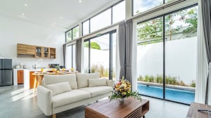 A modern living room with a sofa, coffee table, and a view of a swimming pool through large windows. -  Light Way Villa in Canggu (Canggu)