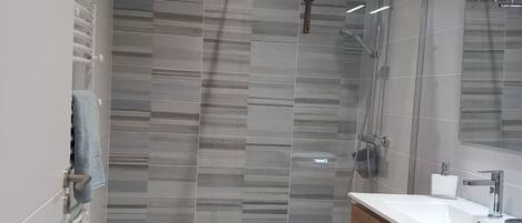 Un baño moderno con cabina de ducha de vidrio, tocador de madera y lavabo blanco.