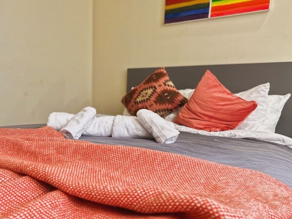 Un lit avec un matelas gris, des oreillers blancs et une couverture rouge à motifs.