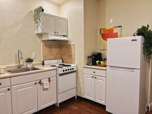 Une cuisine avec des meubles blancs, une cuisinière, un évier et un réfrigérateur.