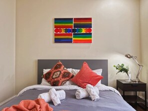 Un lit bien fait, avec des oreillers et des serviettes, une lampe de chevet et une œuvre d’art accrochée au mur.