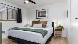 Een slaapkamer met een bed, nachtkastje, lamp en een ingelijst schilderij aan de muur.