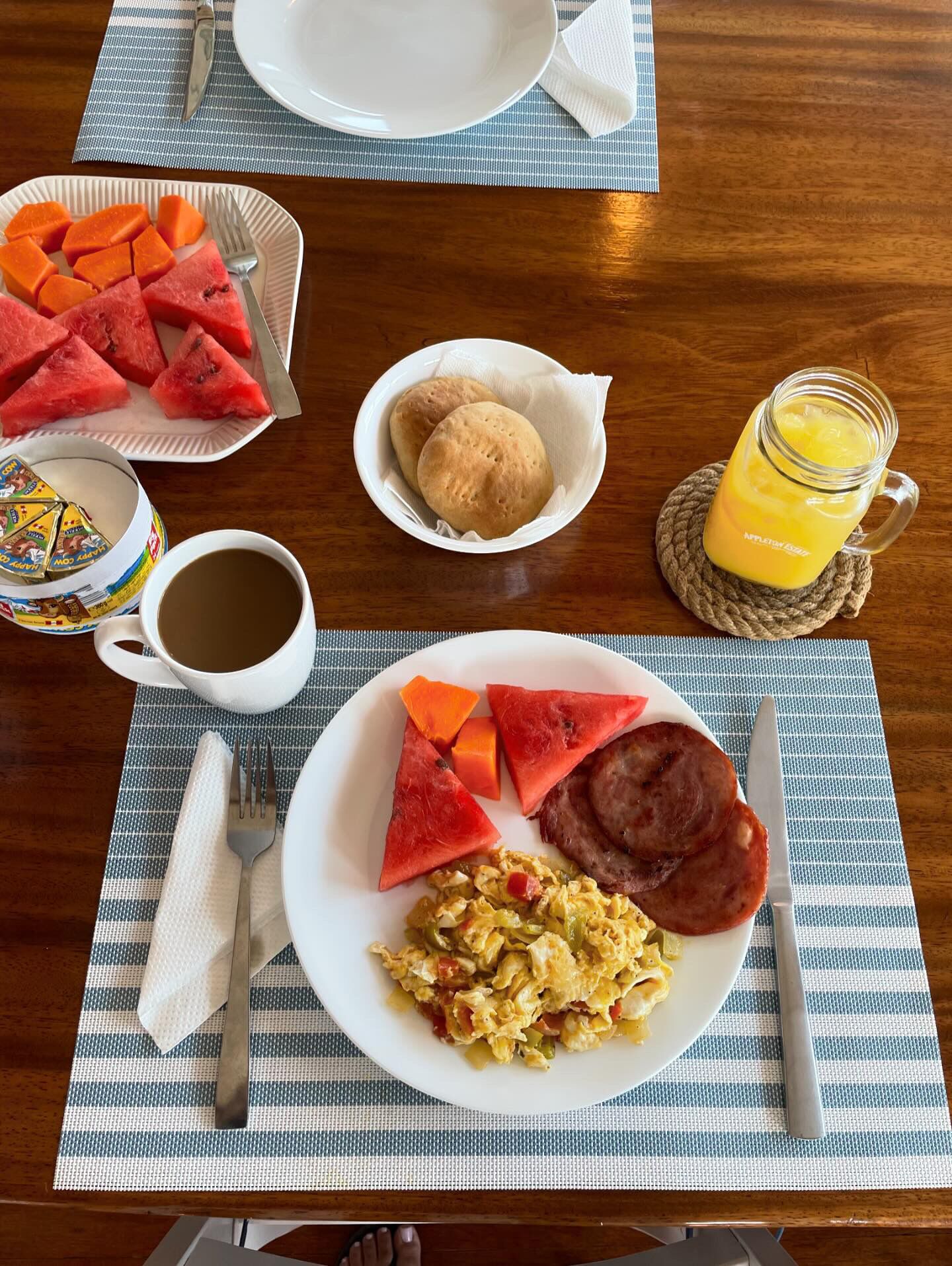 A breakfast table with plates of food, a mug of coffee, and a glass of orange juice.