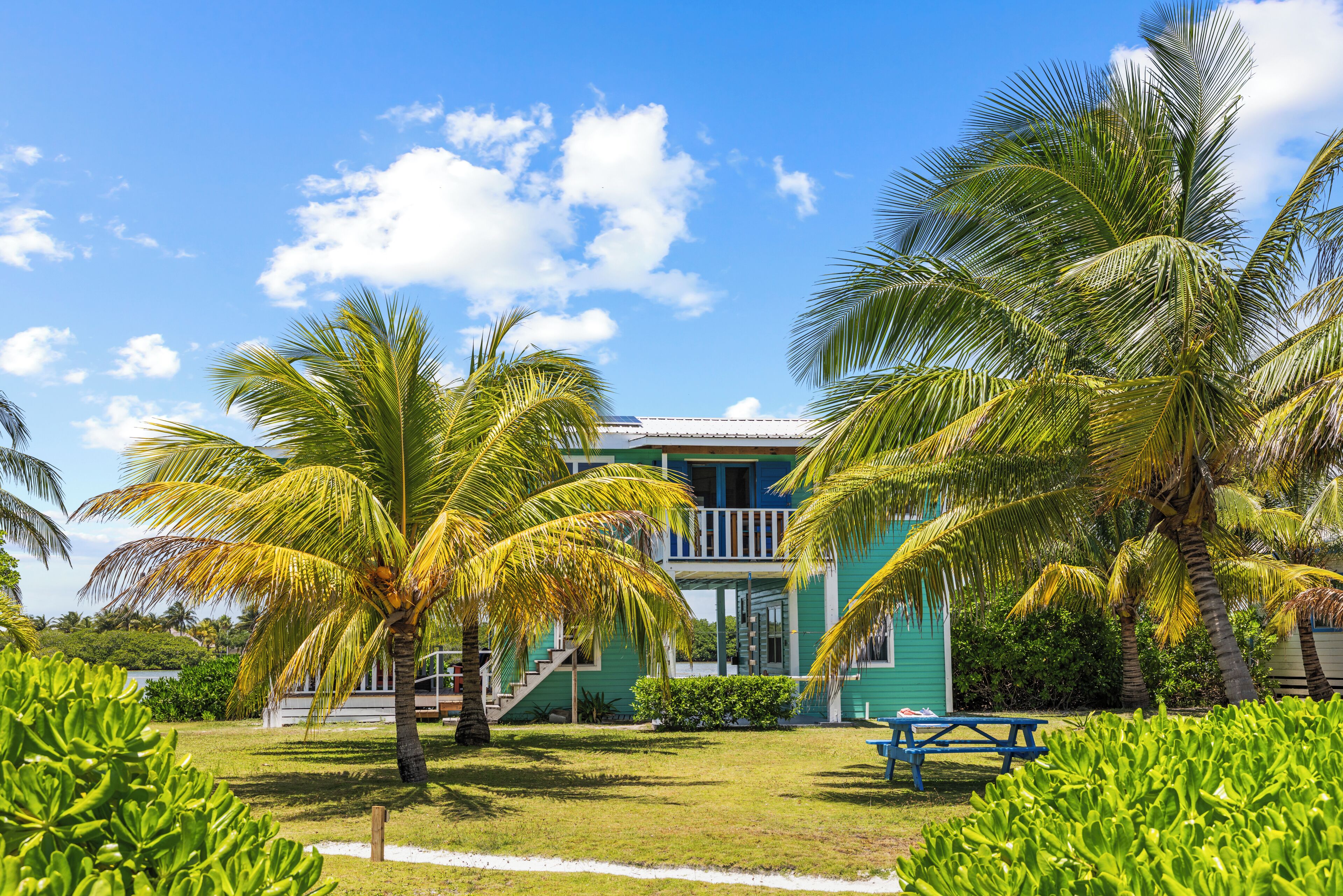 A two-story building with a balcony, surrounded by palm trees and a grassy lawn.