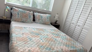 Sängyssä on kuviollinen, meriaiheinen peitto, yöpöydällä on lamppu ja yöpöydän päällä pieni kasvi.