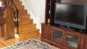 A staircase with wooden steps and black railings, a wooden entertainment center with a flat-screen TV, and a patterned rug on the floor. - Comfortable home in Alexandria, walkable to Old Town / Metro, close to DC (Alexandria)
