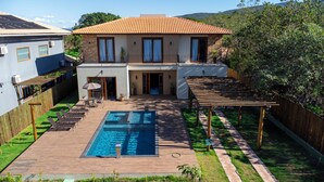 Ein zweistöckiges Haus mit Schwimmbad, überdachter Terrasse und umzäunter Garten.