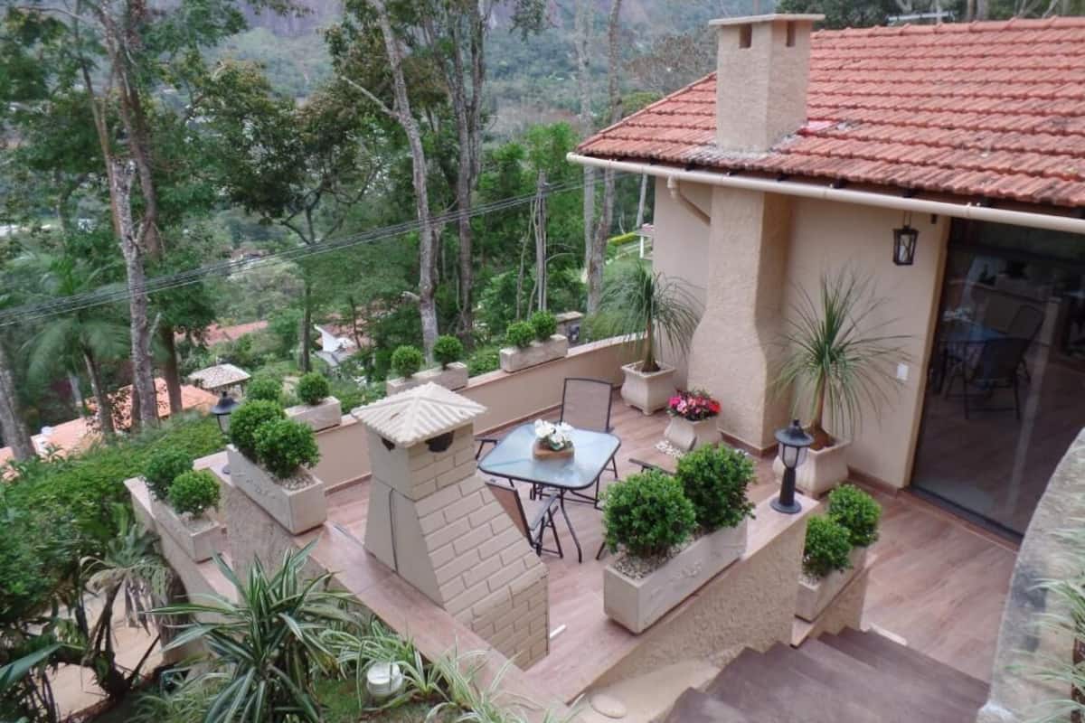 Ein Haus mit einer Terrassenfläche, die einen Tisch und Stühle bietet, umgeben von Topfpflanzen und Blick auf eine Berglandschaft.