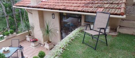 A small house with a tiled roof, a patio with a table and chairs, and potted plants.