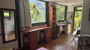 Una habitación acogedora con un escritorio de madera, una cama y vistas a un paisaje verde exuberante a través de grandes ventanales.