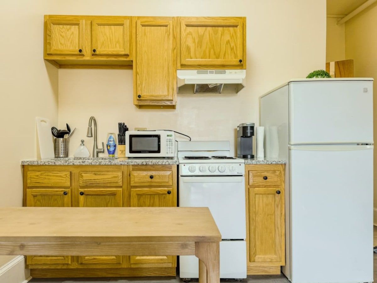 Une cuisine avec des meubles de rangement en bois, une cuisinière, un four à micro-ondes, un réfrigérateur et une table.
