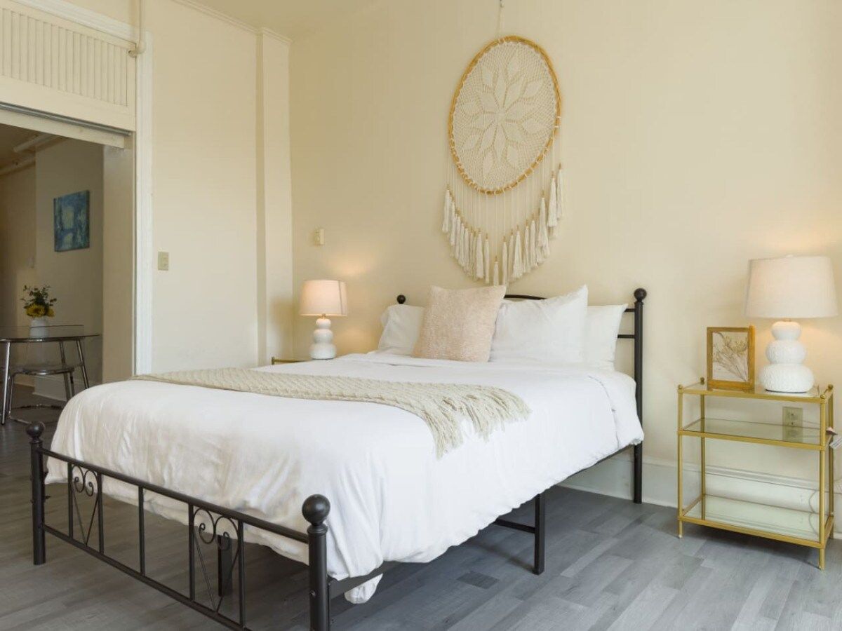 A bedroom with a bed, bedside lamps, a wall hanging, and a small table with a lamp.