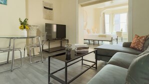 Una sala de estar moderna con una mesa de centro de vidrio, un sofá, un televisor y un comedor con sillas.