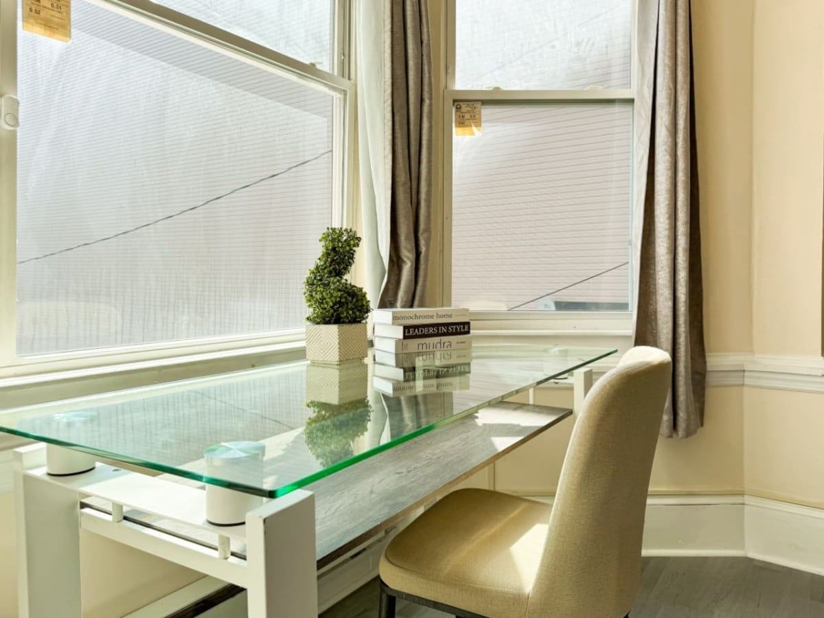 A modern room with a glass table, a chair, a small plant, and books.