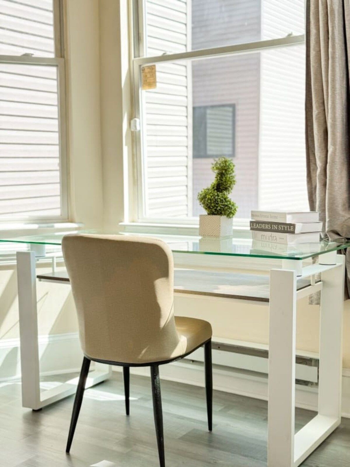 A modern room with a glass desk, a beige chair, and a small potted plant.