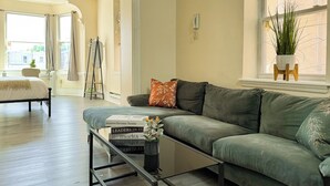 Un salón espacioso con un sofá verde, una mesa de centro con libros y una ventana con una planta.