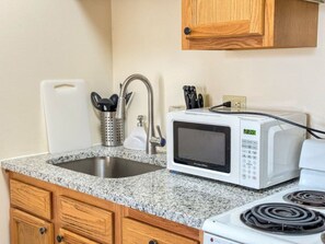 Una cocina con encimeras de granito, un lavamanos de acero inoxidable, un microondas blanco y una estufa.