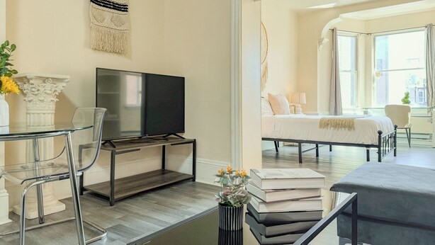Una sala de estar moderna con una mesa de centro de vidrio, un televisor de pantalla plana, una estantería y una cama con vistas a la ciudad.