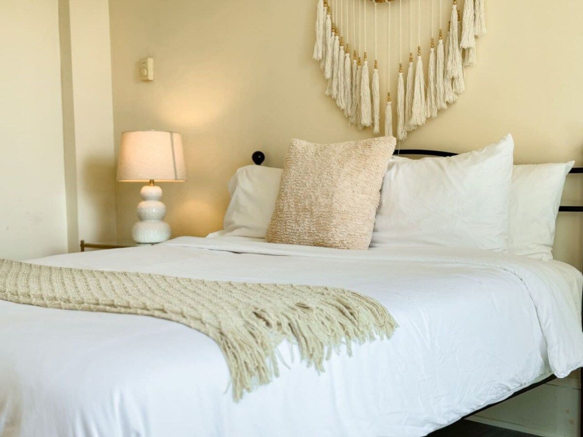 Un lit bien fait, avec du linge de lit blanc et un plaid beige.