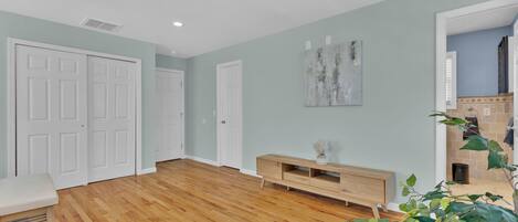 A spacious living room with hardwood flooring, white doors, a wooden bench, a console table, and a ceiling fan.