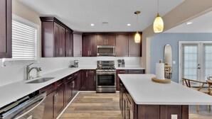 A modern kitchen with dark wood cabinets, stainless steel appliances, a white countertop, and a hanging pendant light.