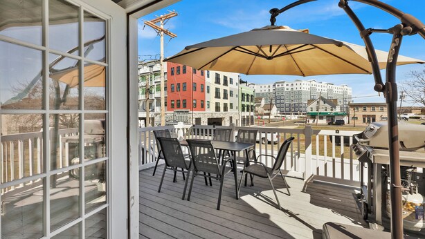 A deck with outdoor furniture and a grill, overlooking a cityscape with colorful buildings.