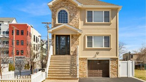 A two-story residential building with a stone facade, a front entrance with steps, and a garage.