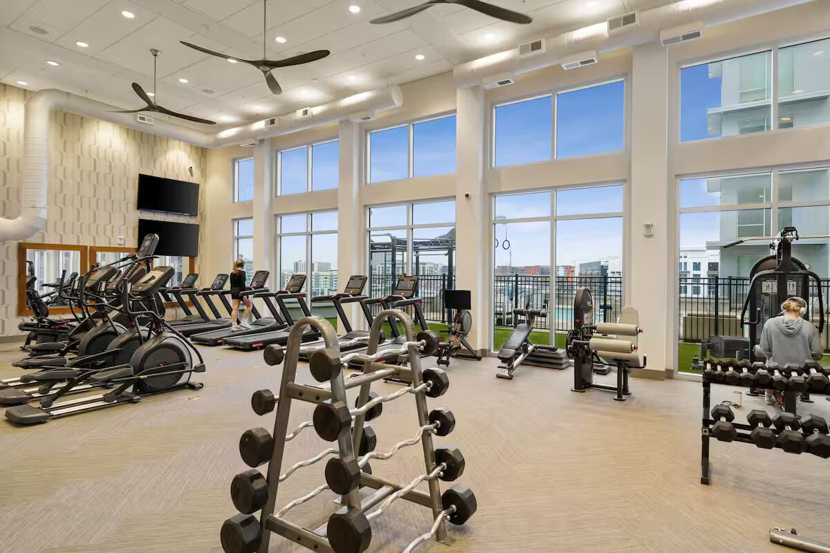 Een ruime fitnessruimte met loopbanden, krachtapparaten en een dumbbells rek.