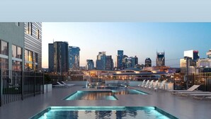 Piscina no terraço com vista para a cidade, cadeiras de descanso e edifícios modernos ao fundo.
