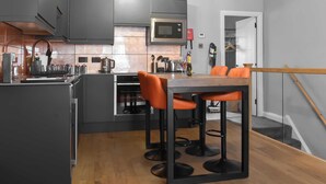 A modern kitchen with grey cabinets, a stainless steel microwave, and a wooden dining table with orange chairs. - 1 bedroom accommodation in Windermere (Windermere)