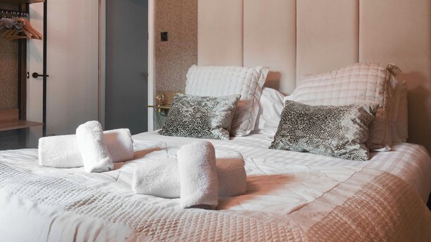A neatly made bed with white and patterned pillows, a quilted blanket, and two folded towels. - 1 bedroom accommodation in Windermere (Windermere)