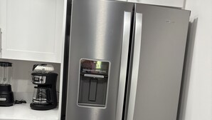 Ein Edelstahl-Kühlschrank von Whirlpool mit Wasserspender und Eiswürfelbereiter, eine Kaffeemaschine und ein Mixer auf der Arbeitsplatte.
