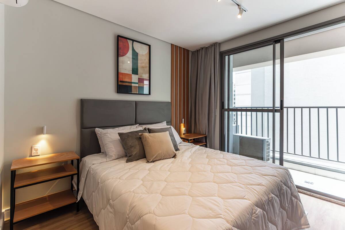 Un dormitorio moderno con una cama grande, cabecera, mesitas de noche, ventana con vistas y un cuadro en la pared.