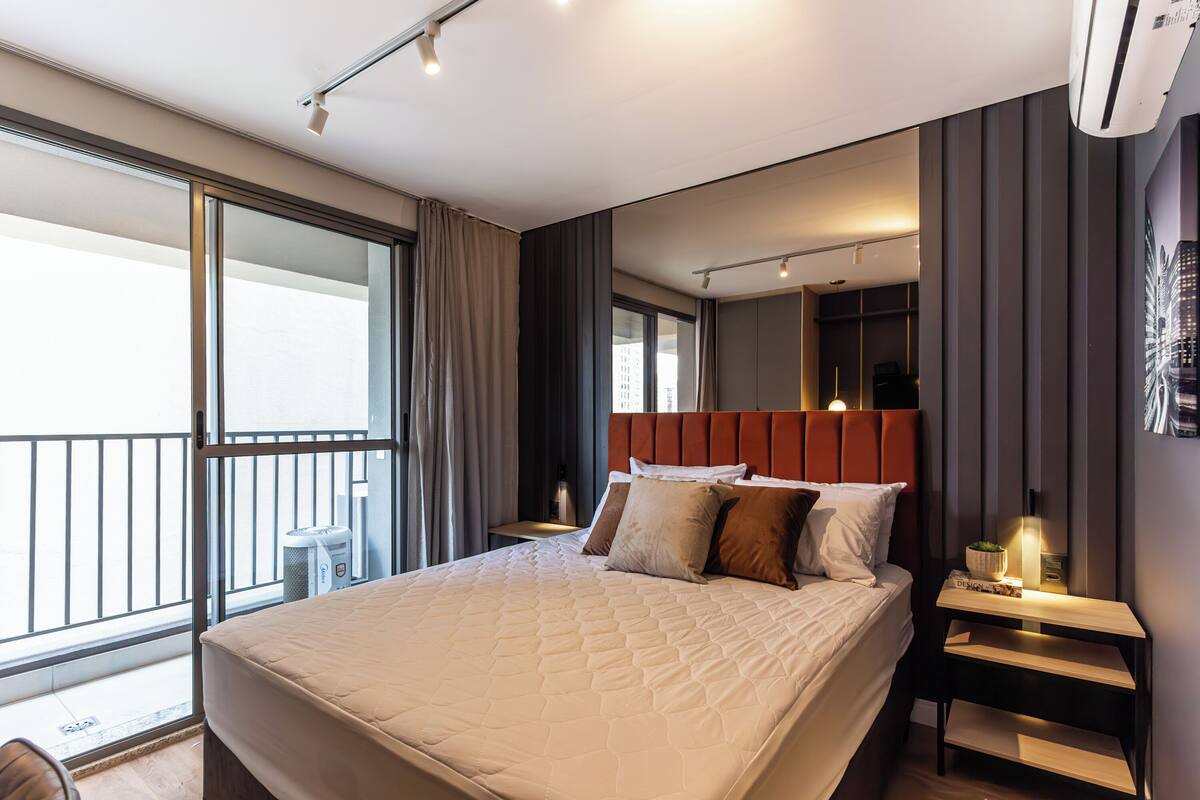 Una habitación de hotel moderna con una cama grande, una mesita de noche, una pequeña mesa y un amplio ventanal con cortinas.