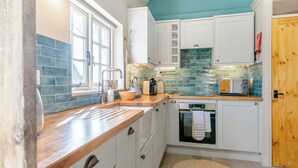A compact kitchen with white cabinets, a wooden countertop, a blue-tiled backsplash, and a built-in oven. - 3 bedroom accommodation in Wedmore, near Glastonbury (Wedmore, near Glastonbury)