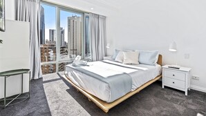 Quarto de hotel moderno com uma cama grande, mesa de cabeceira e vista para a paisagem urbana através de amplas janelas.