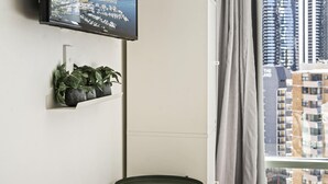 Quarto moderno com televisão na parede, uma pequena mesa e um aparador de plantas.
