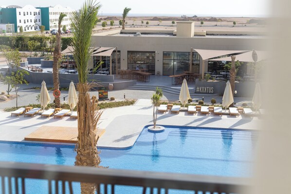 Zona de piscina amb gandules i ombrelles, restaurant amb terrassa i vistes al desert al fons.